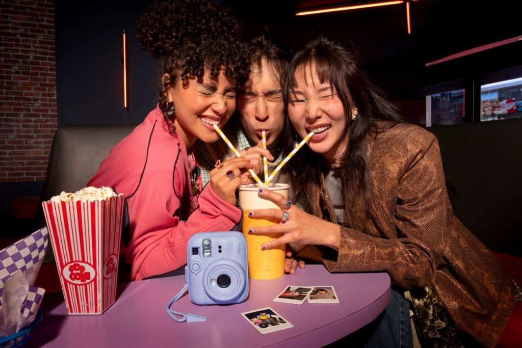 a group of friends sharing a milkshake with a Dreamy Purple instax mini 13™ instant camera on the table infront of them