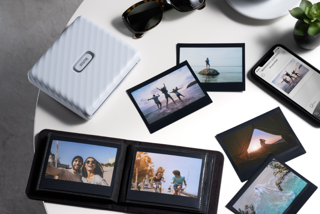 instax Link WIDE™ smartphone printer on a table surrounded by instax™ WIDE prints on black film