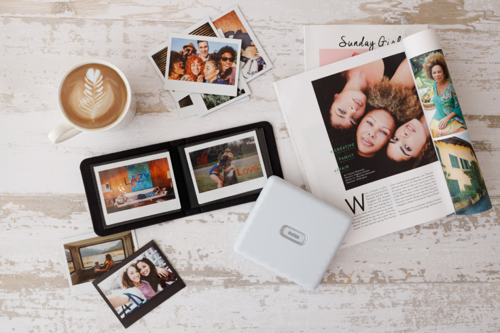instax™ WIDE photo album sat on a coffee table surrounded by instax™ WIDE prints and an instax™ Link WIDE smartphone printer